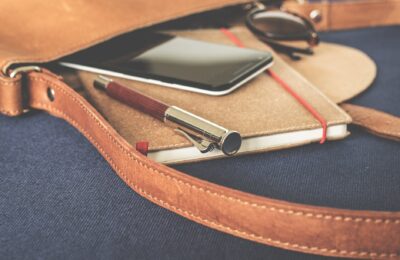 smartphone displaying black screen on notebook beside pen and sunglasses