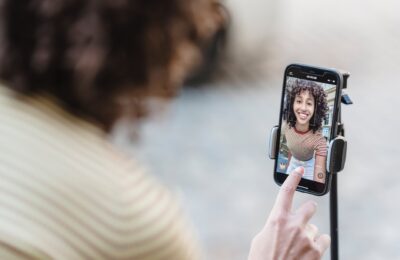 crop smiling ethnic blogger recording video on smartphone on street